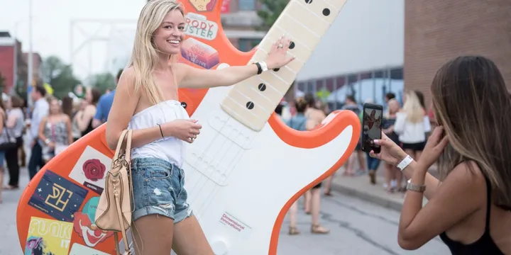 A festival attendee playing a giant illuminated electric guitar