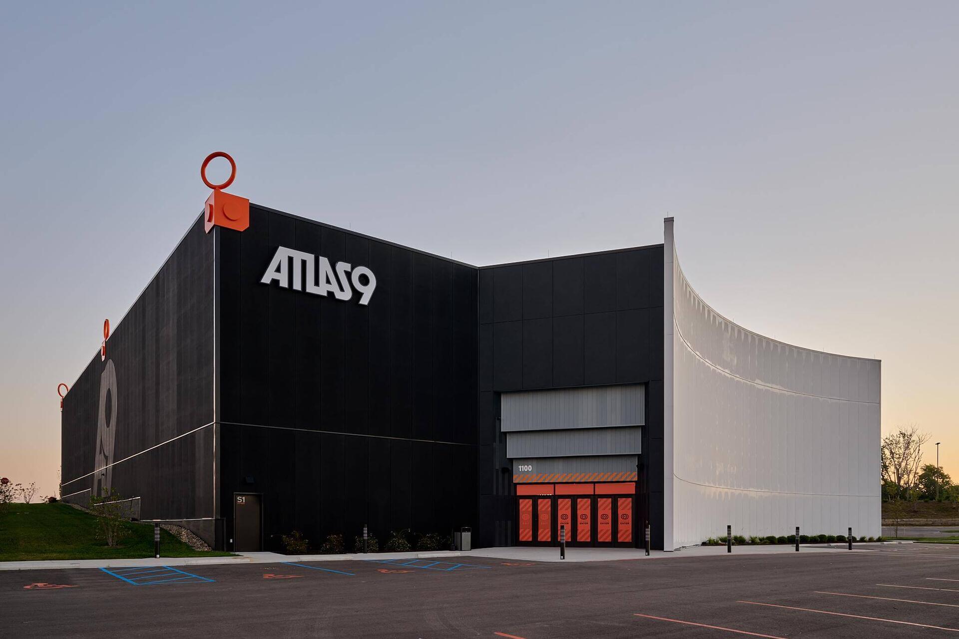 Exterior of the Atlas9 building at dusk, with the logo on a black facade and a sweeping white curved wall