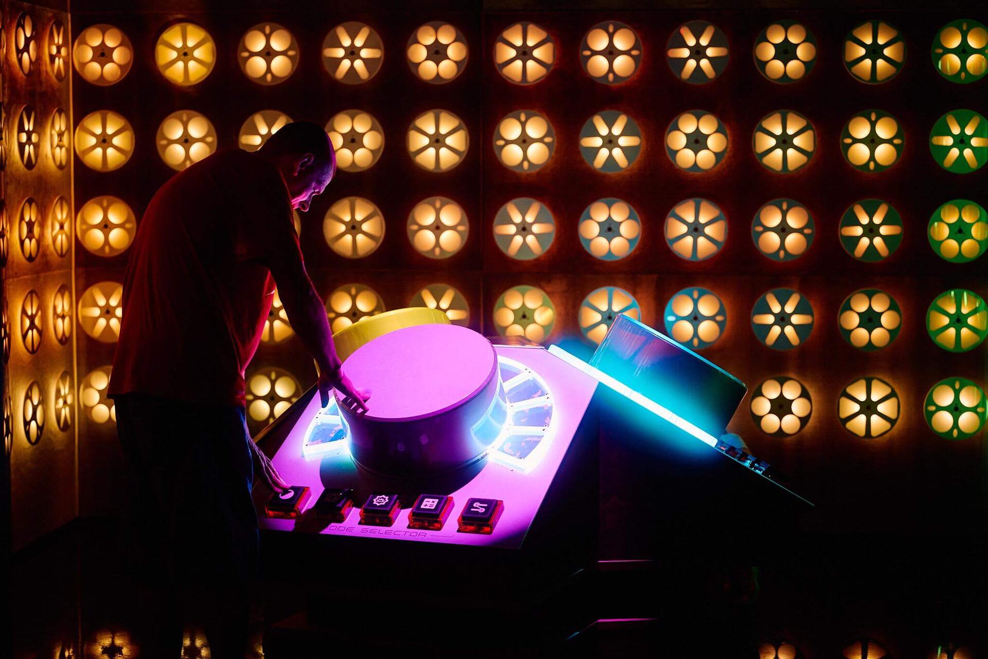 A visitor operating a glowing control table in front of a wall of amber flower-shaped lights