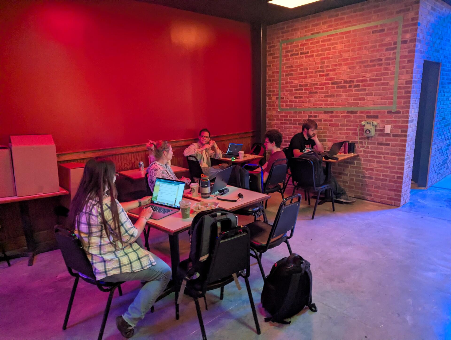 The team working on laptops around tables in a red-walled room during production